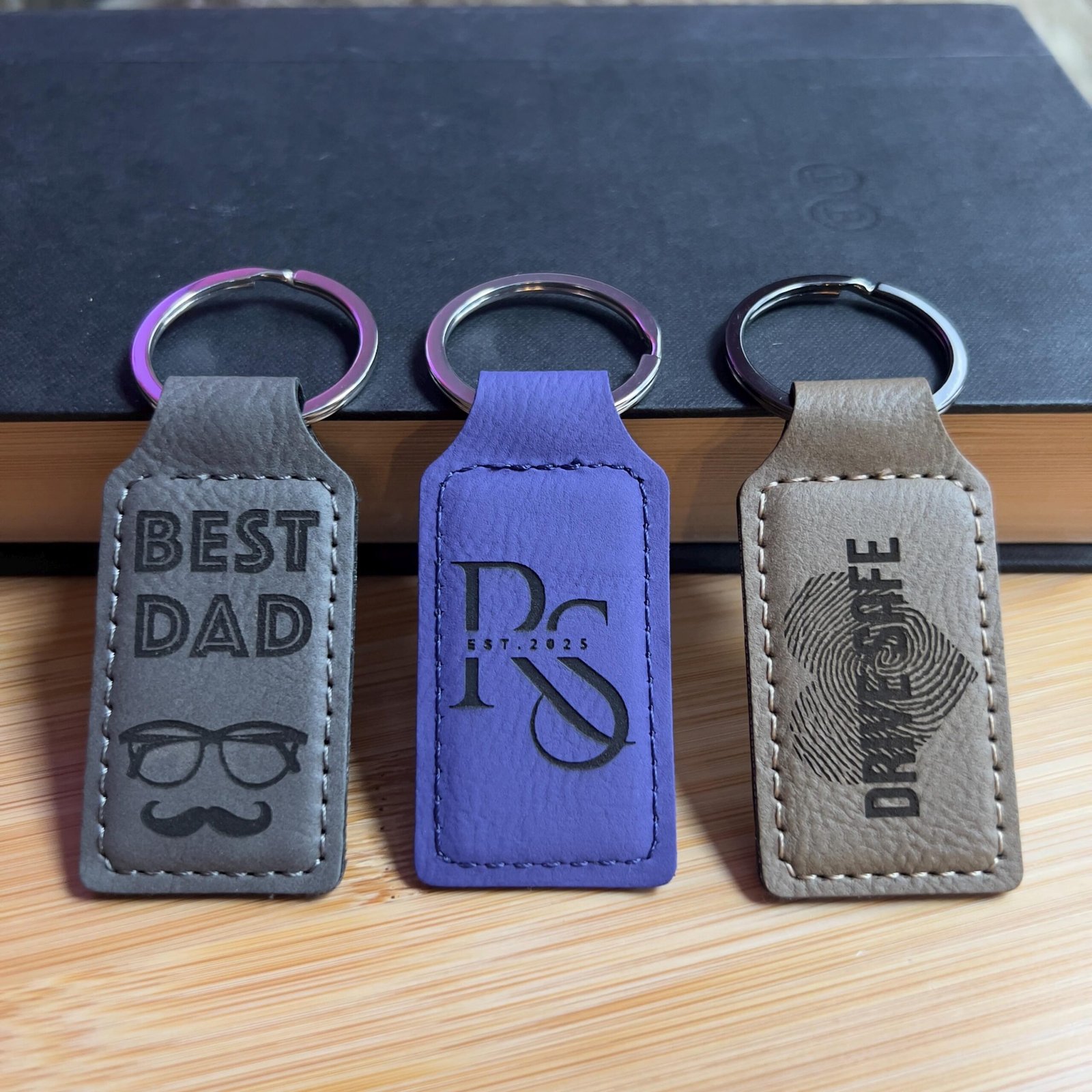 Gray, purple and tan vegan leatherette keychains engraved with Best Dad, an RS monogram and Drive Safe