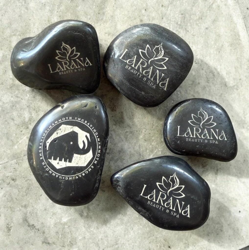 Black river rocks engraved with lotus logo and mammoth emblem