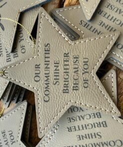 Close view of a gray leatherette star ornament engraved with Our Communities Shine Brighter Because Of You