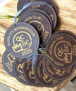 Round brown leatherette ornaments engraved with a gold bourbon club logo and 2025