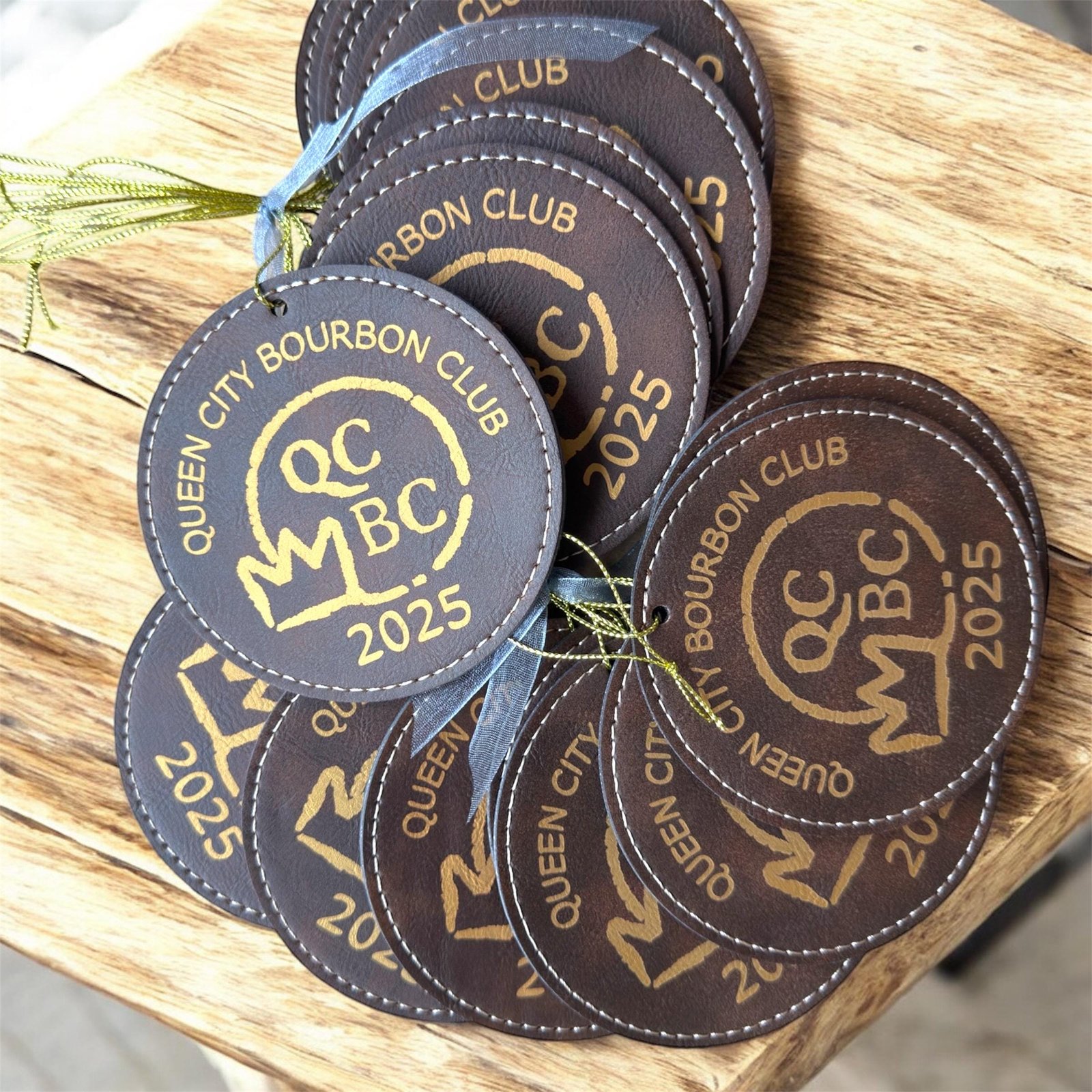 Round brown leatherette ornaments engraved with a gold bourbon club logo and 2025