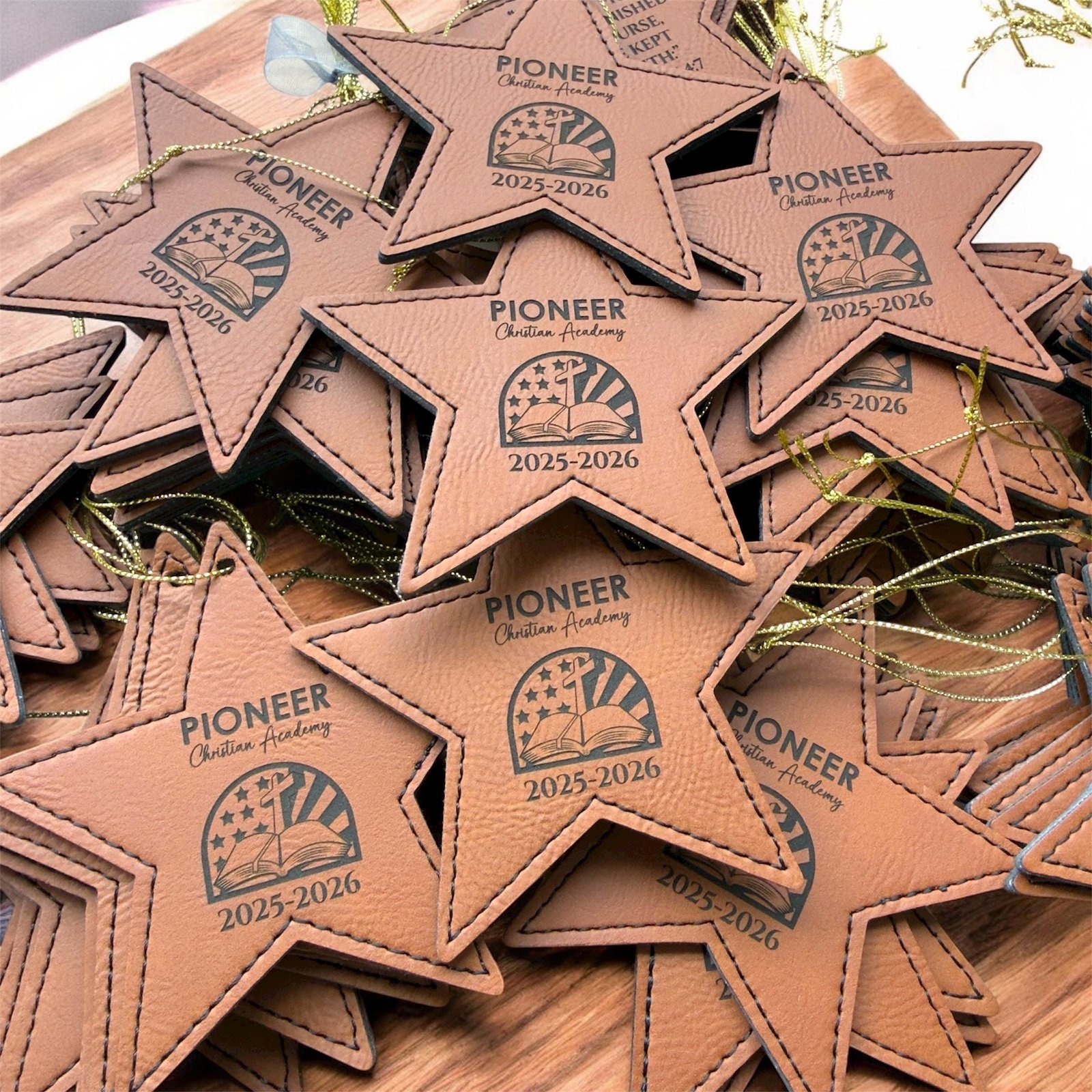 Brown leatherette star Christmas ornaments engraved with a sample Pioneer academy logo and years