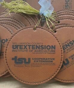 Large brown round leatherette ornament engraved with a sample extension logo, stacked with others