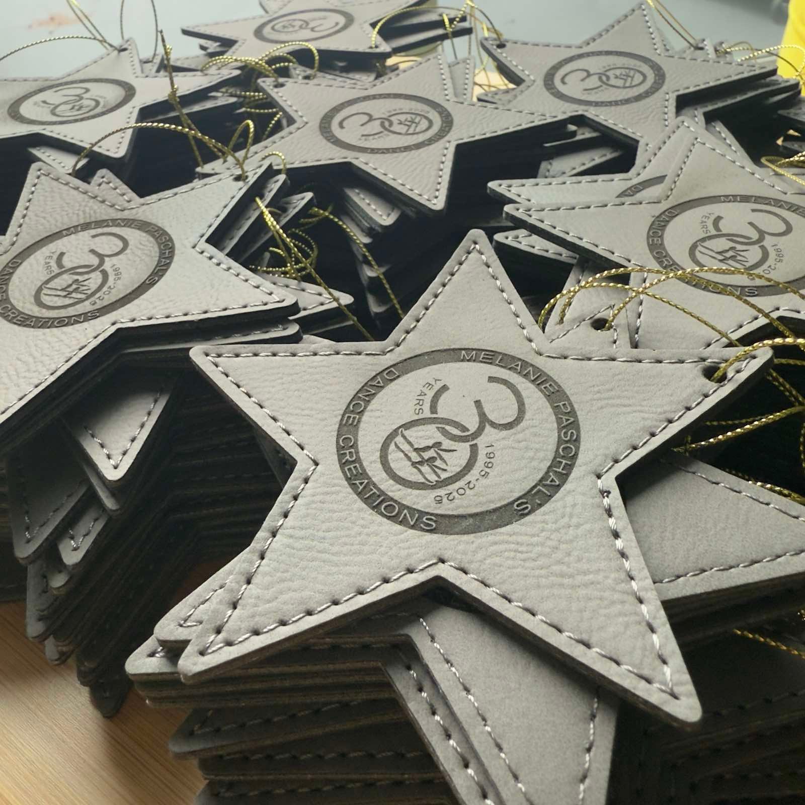 Gray leatherette star ornament with a circular sample logo on top of a pile of black star ornaments